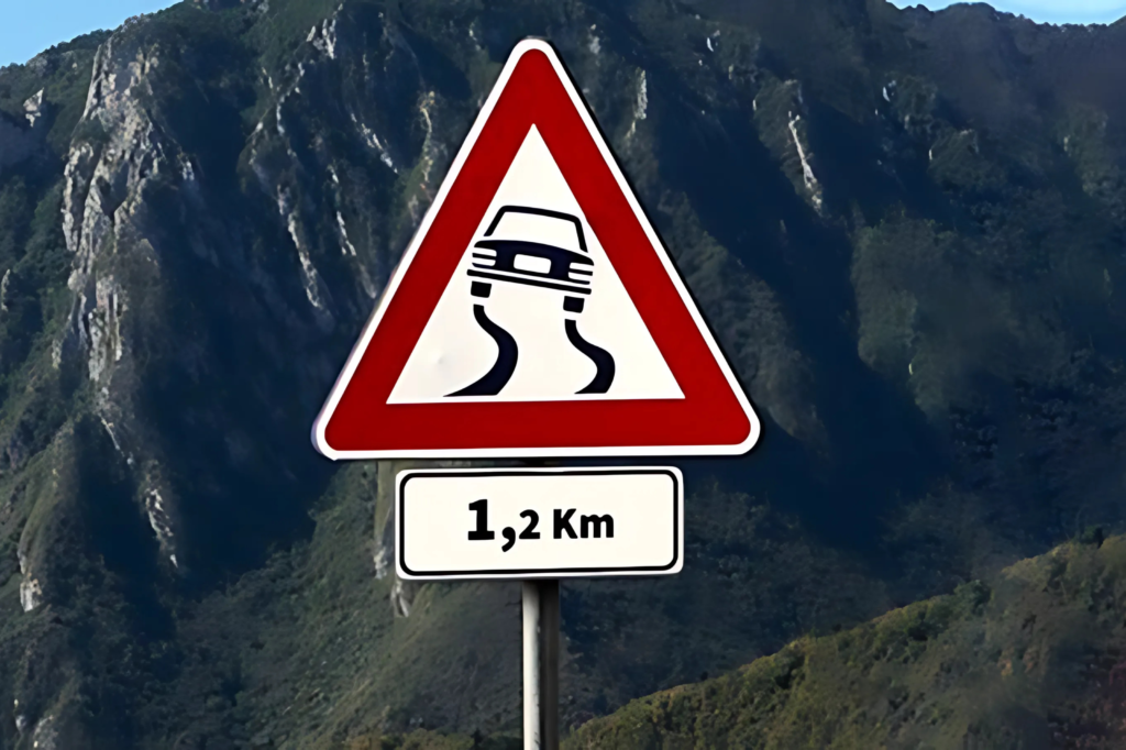 Un cartello stradale che contiene un pannello integrativo che indica che c'è un tratto di strada scivoloso in caso di avverse condizioni del tempo (neve, ghiaccio o pioggia) per 1,2 Km